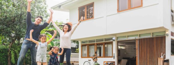 a family is standing in front of a house with their arms in the air .