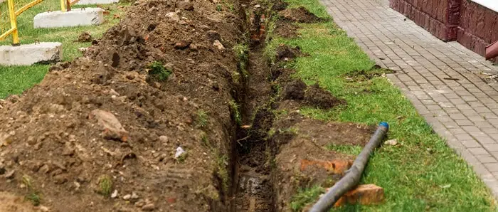 a trench is being dug in the grass next to a sidewalk .
