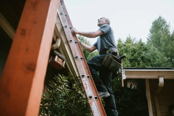 A man is climbing a ladder to fix a gutter on the side of a house .