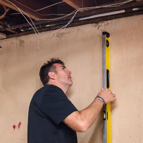 a man is using a level to measure a wall in a basement .