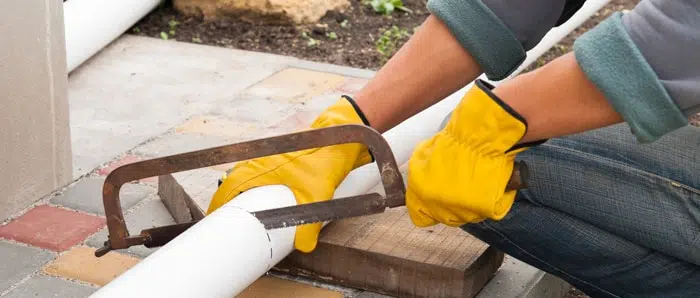 a man is cutting a pipe with a hacksaw.