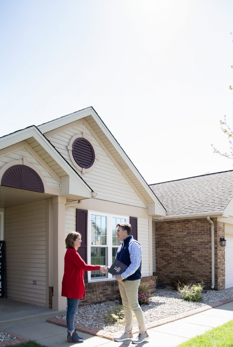 a woman shakes hands with a male Helitech employee in front of a house with a welcome sign