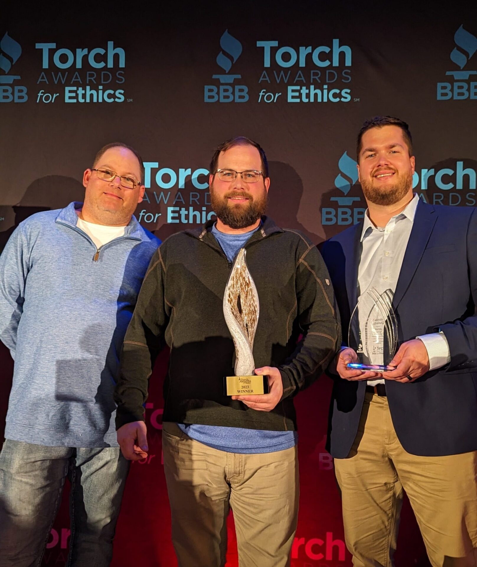 three men standing in front of a wall that says torch awards for ethics